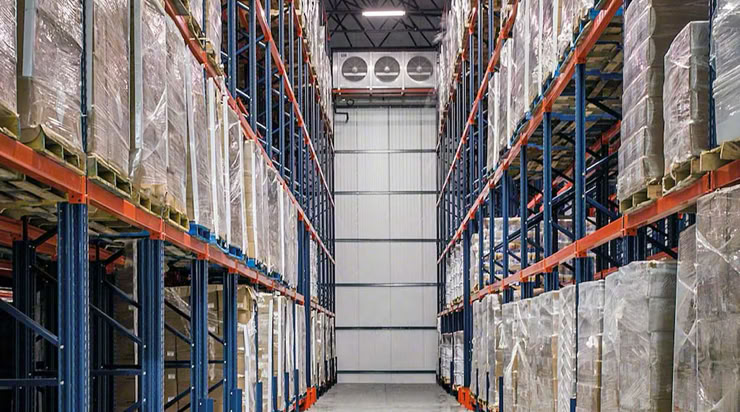 Warehouse interior with tall shelves stacked with wrapped pallets on both sides of a central aisle.